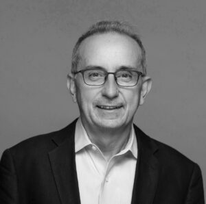 Black and white portrait of a man wearing glasses and a suit jacket.